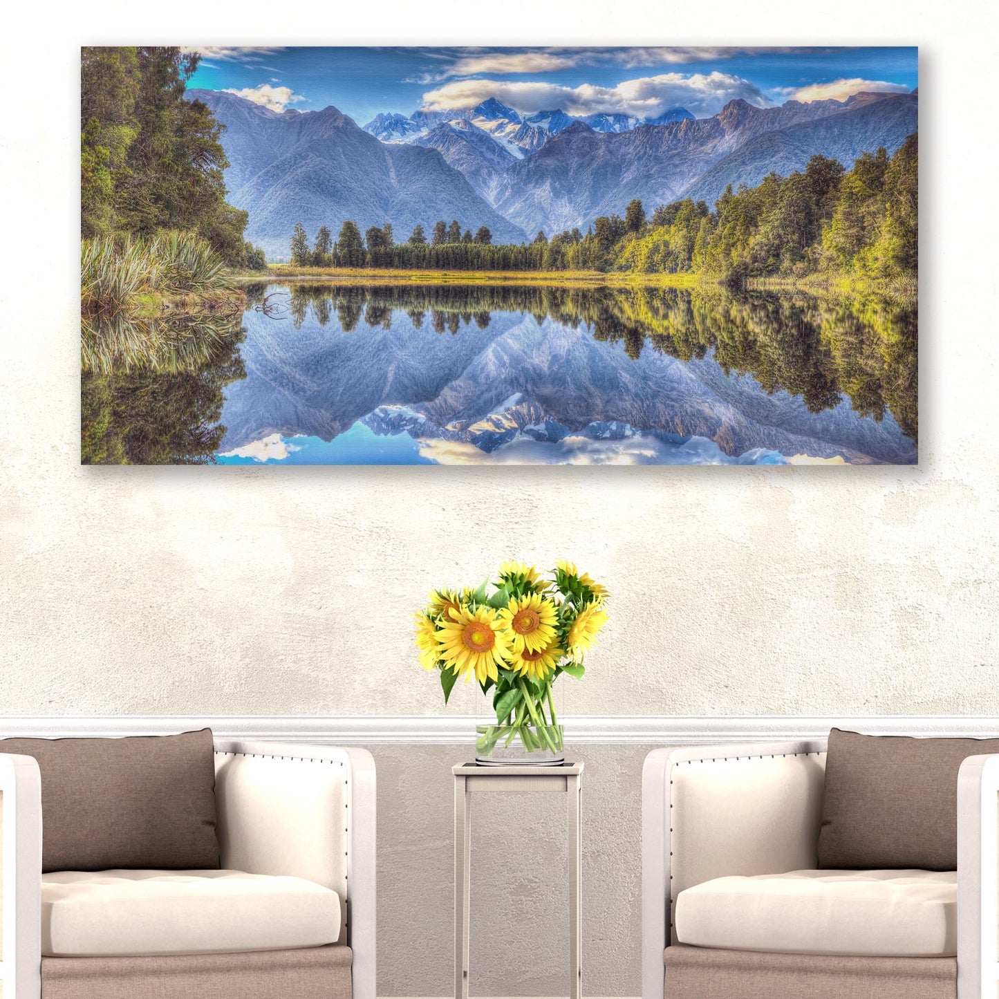 Landscape painting of a mountain lake with a vase of sunflowers on a table below.