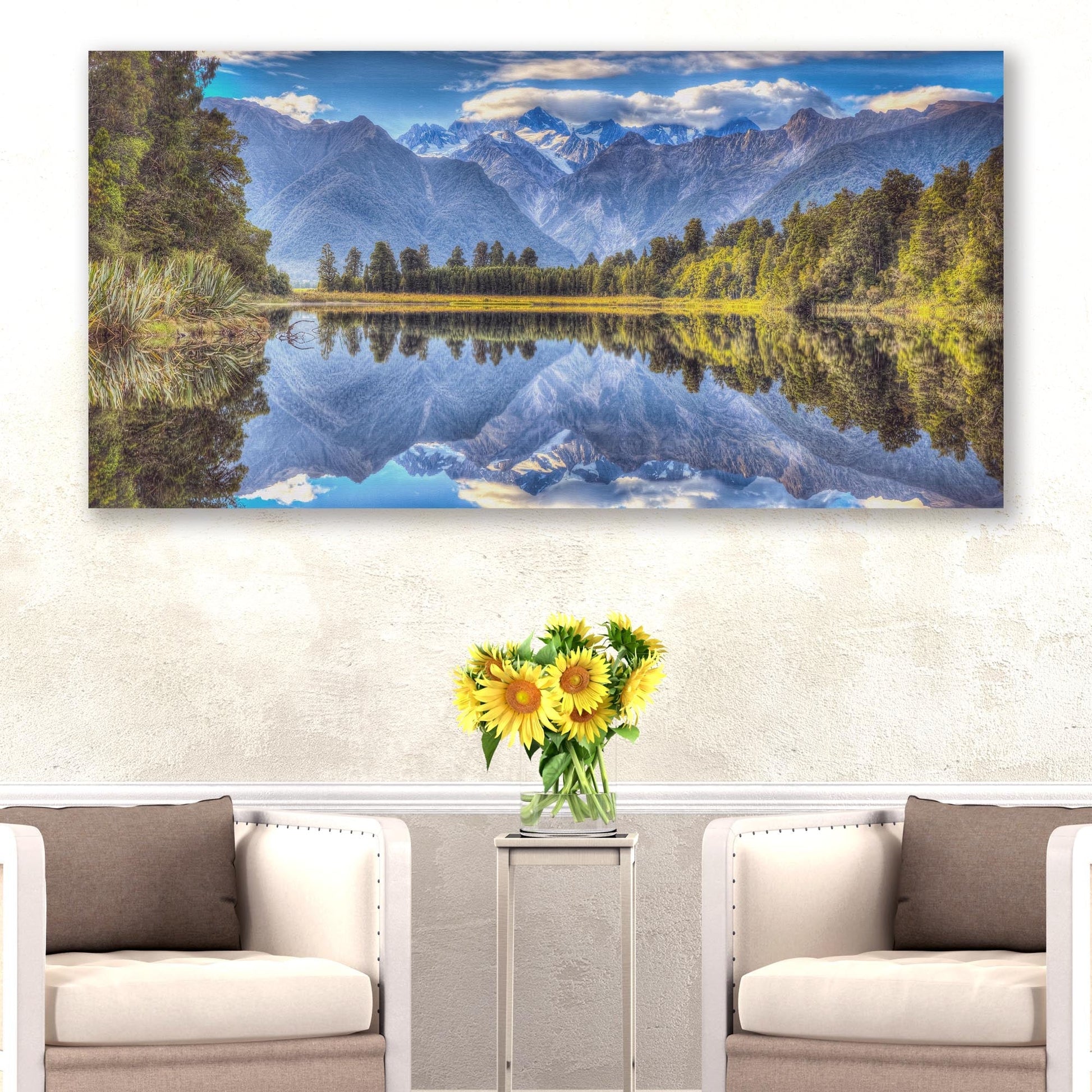 Landscape painting of a mountain lake with a vase of sunflowers on a table below.