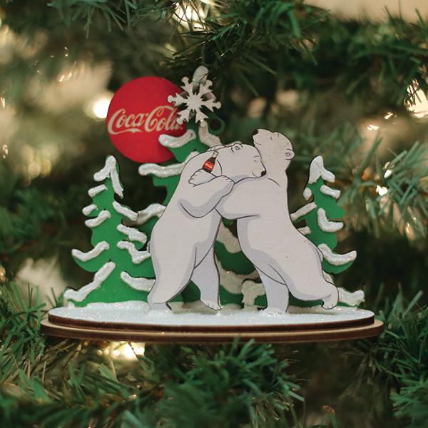 Christmas ornament with two bears and a Coca-Cola label on a decorated tree.