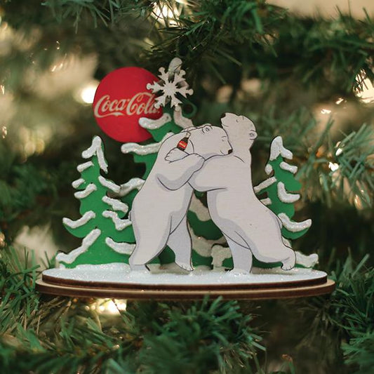 Christmas ornament with two bears and a Coca-Cola label on a decorated tree.