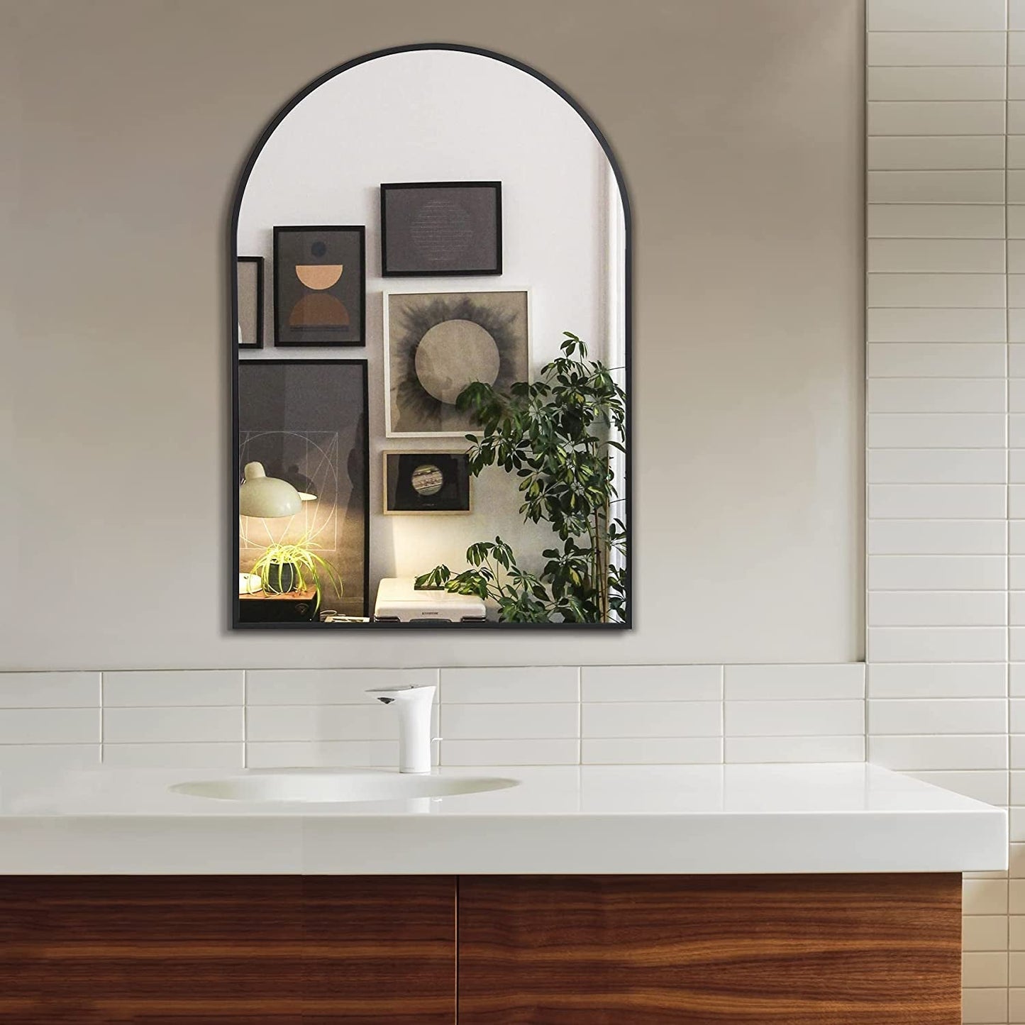 Bathroom with a large arched mirror above a sink, featuring decorative frames and plants.