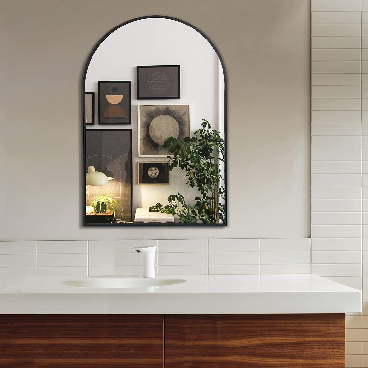 Bathroom with a large arched mirror above a sink, featuring decorative frames and plants.