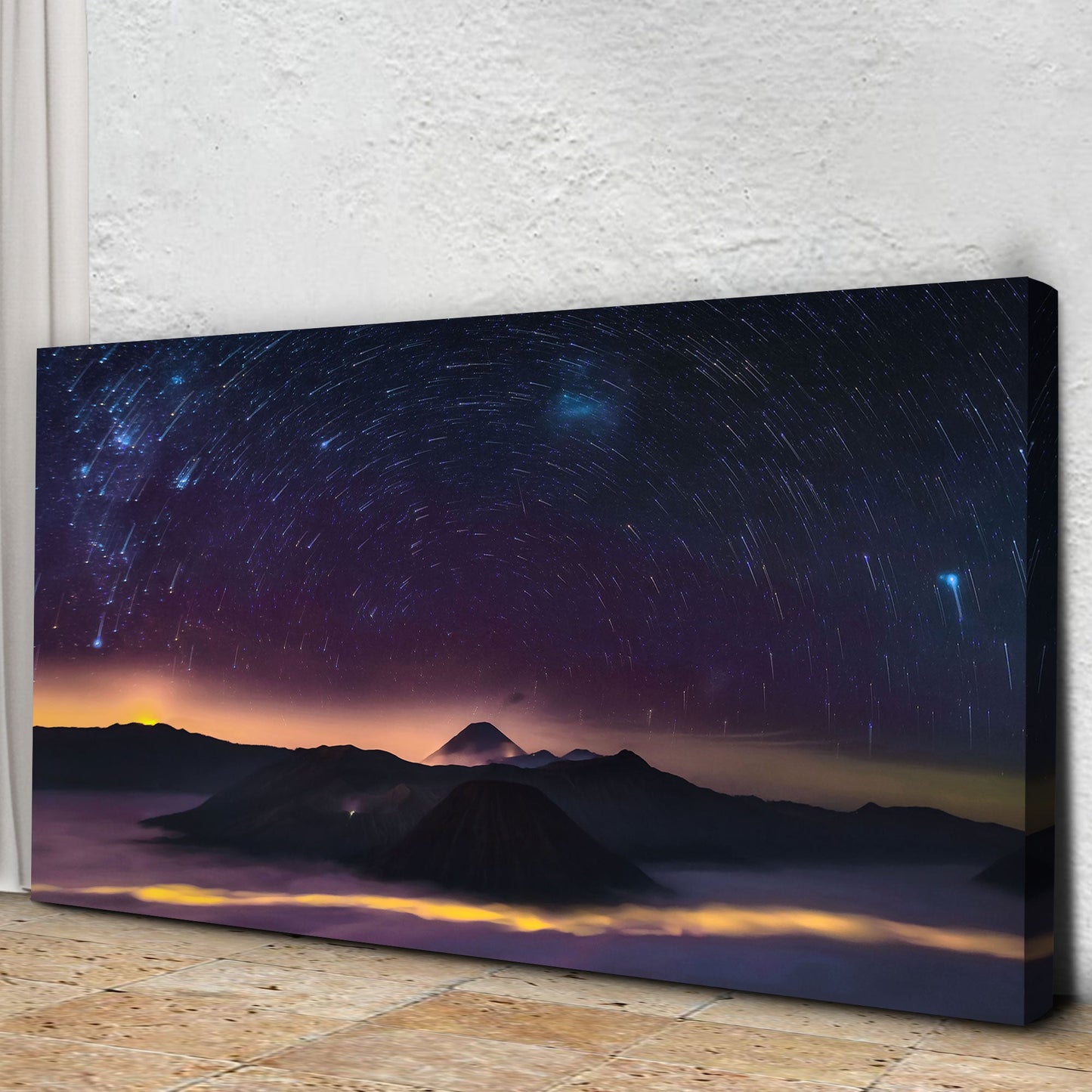 Canvas print of a starry night sky over mountains on a textured wall.