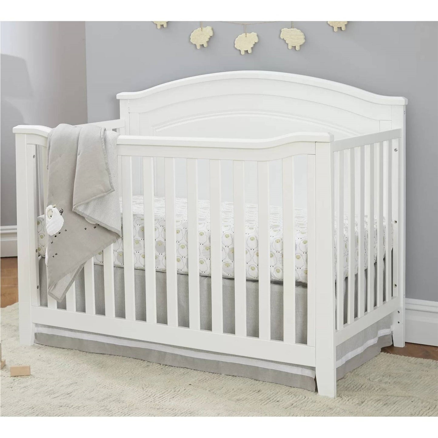 White crib with gray bedding in a room with gray walls and wooden flooring.