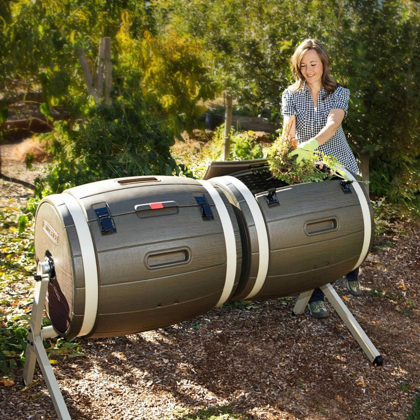 Woman using a large cylindrical compost bin outdoors.
