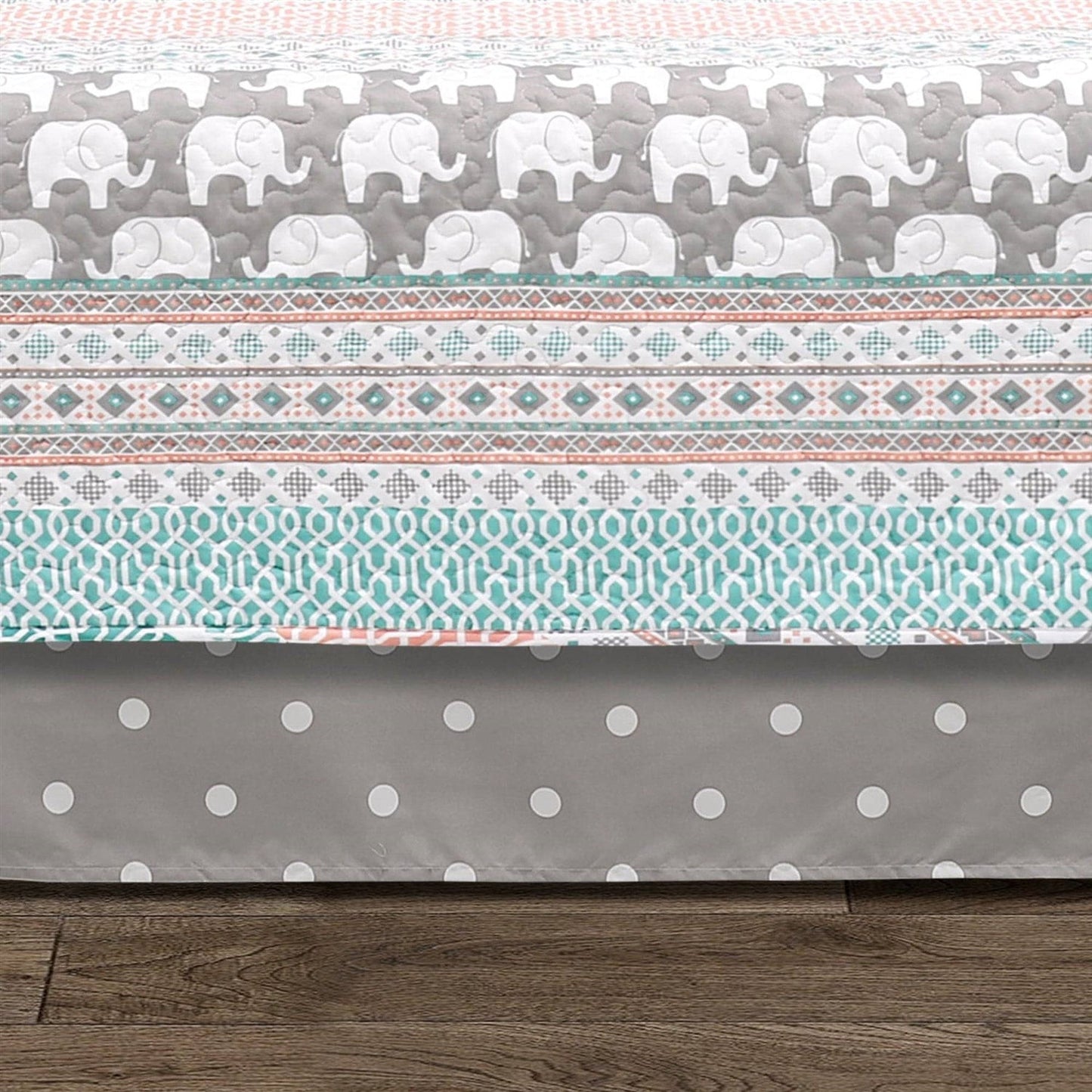 Crib sheet with elephant pattern on top and polka dot pattern at the bottom, on a wooden floor.