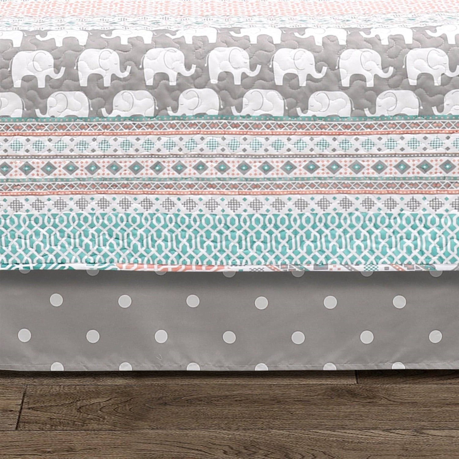 Crib sheet with elephant pattern on top and polka dot pattern at the bottom, on a wooden floor.