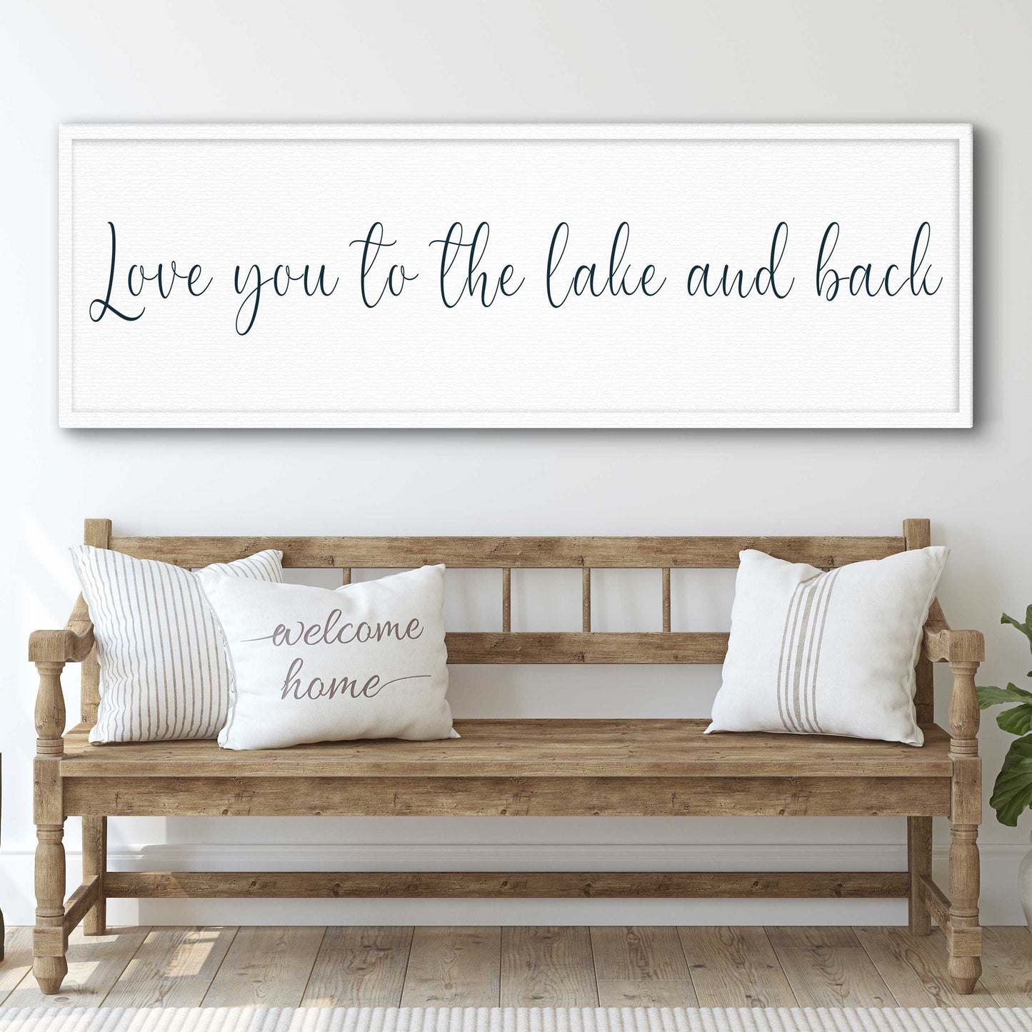 Wooden bench with pillows and a framed quote above on a white wall.