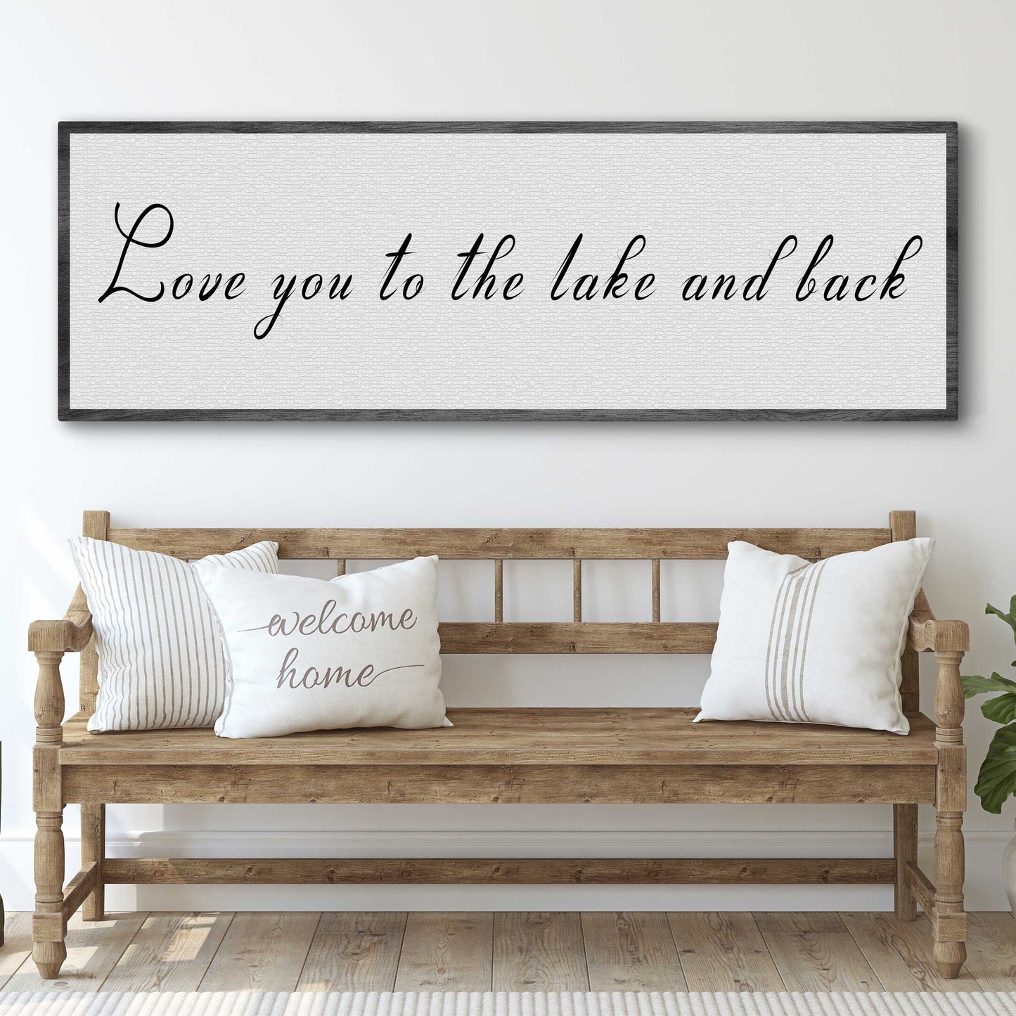Wooden bench with pillows and a framed sign above it in a room.