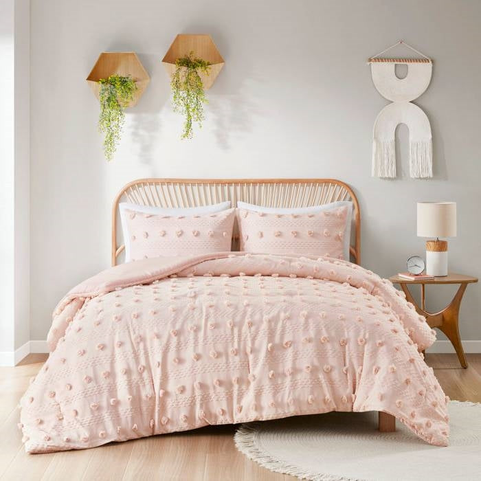 Pink textured comforter set on a bed in a bedroom with decorative elements.