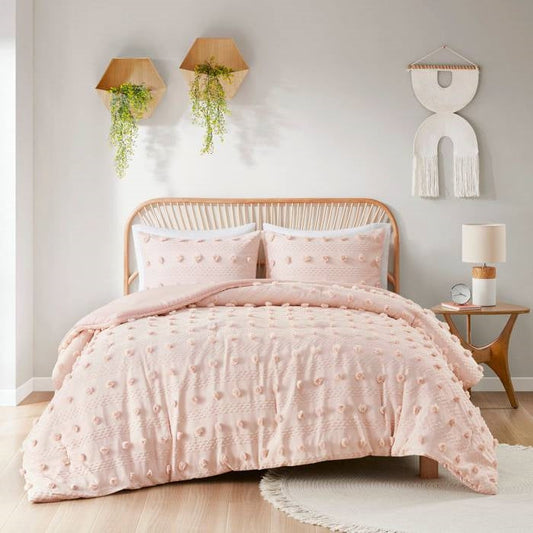 Pink textured comforter set on a bed in a bedroom with decorative elements.