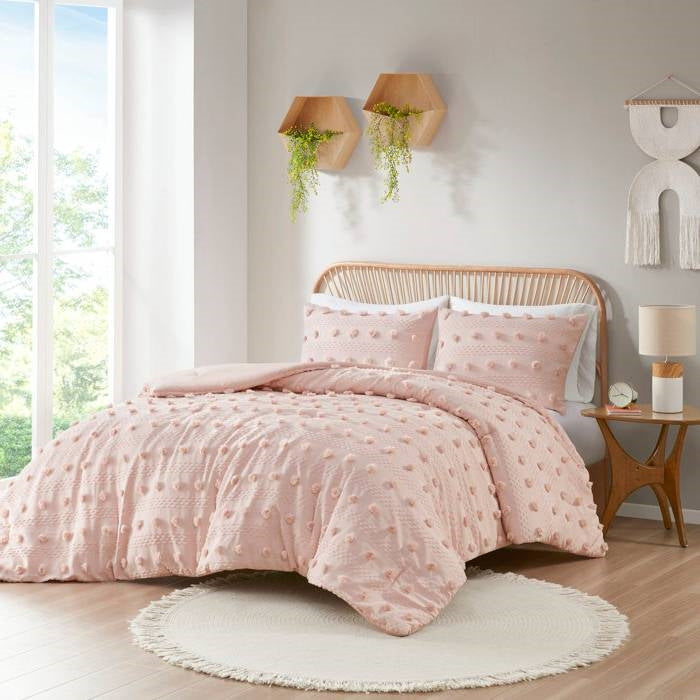 Pink textured comforter set on a bed in a bright bedroom with natural light.