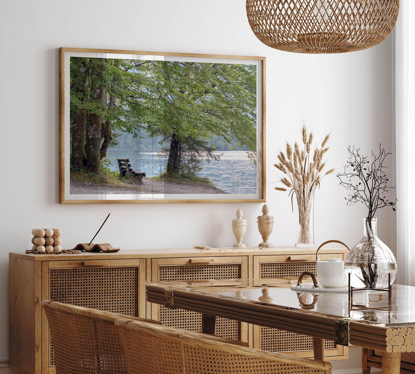 Framed serene lake print of a tranquil lake with a bench under leafy trees, enhancing a modern dining room.