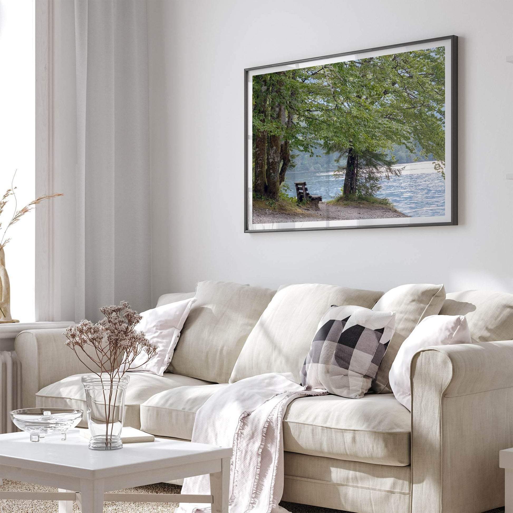 Framed serene lake print of a tranquil lake with a bench under leafy trees, enhancing a modern dining room.