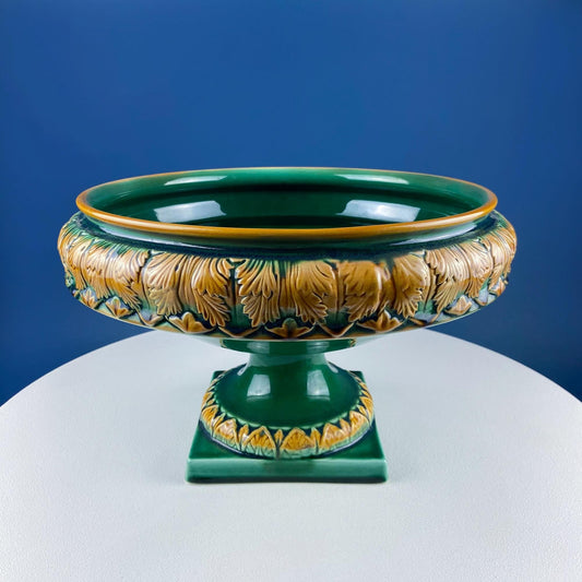 Decorative green and gold ceramic bowl on a white pedestal against a blue background