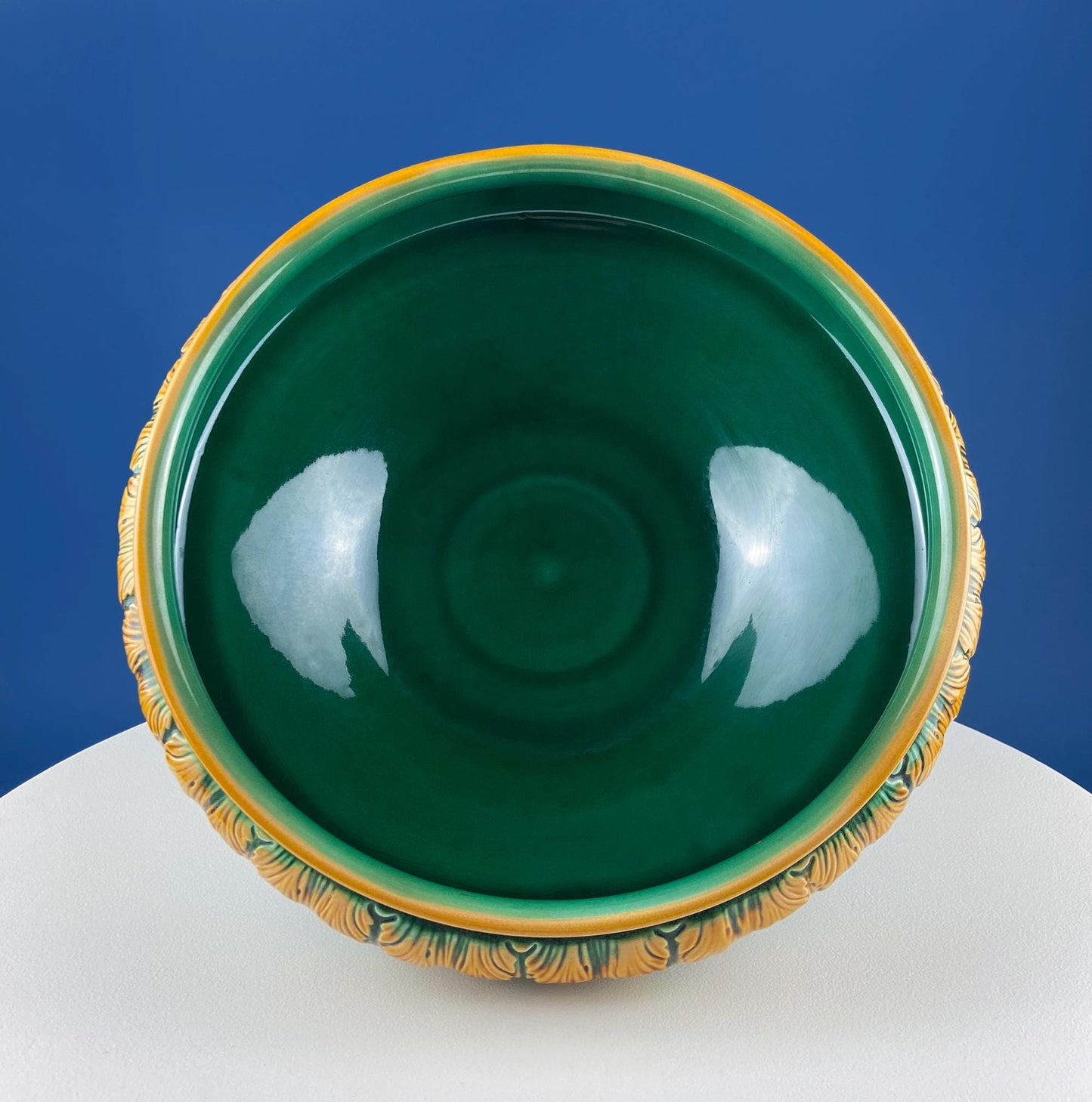 Green ceramic bowl with gold rim on a white pedestal against a blue background