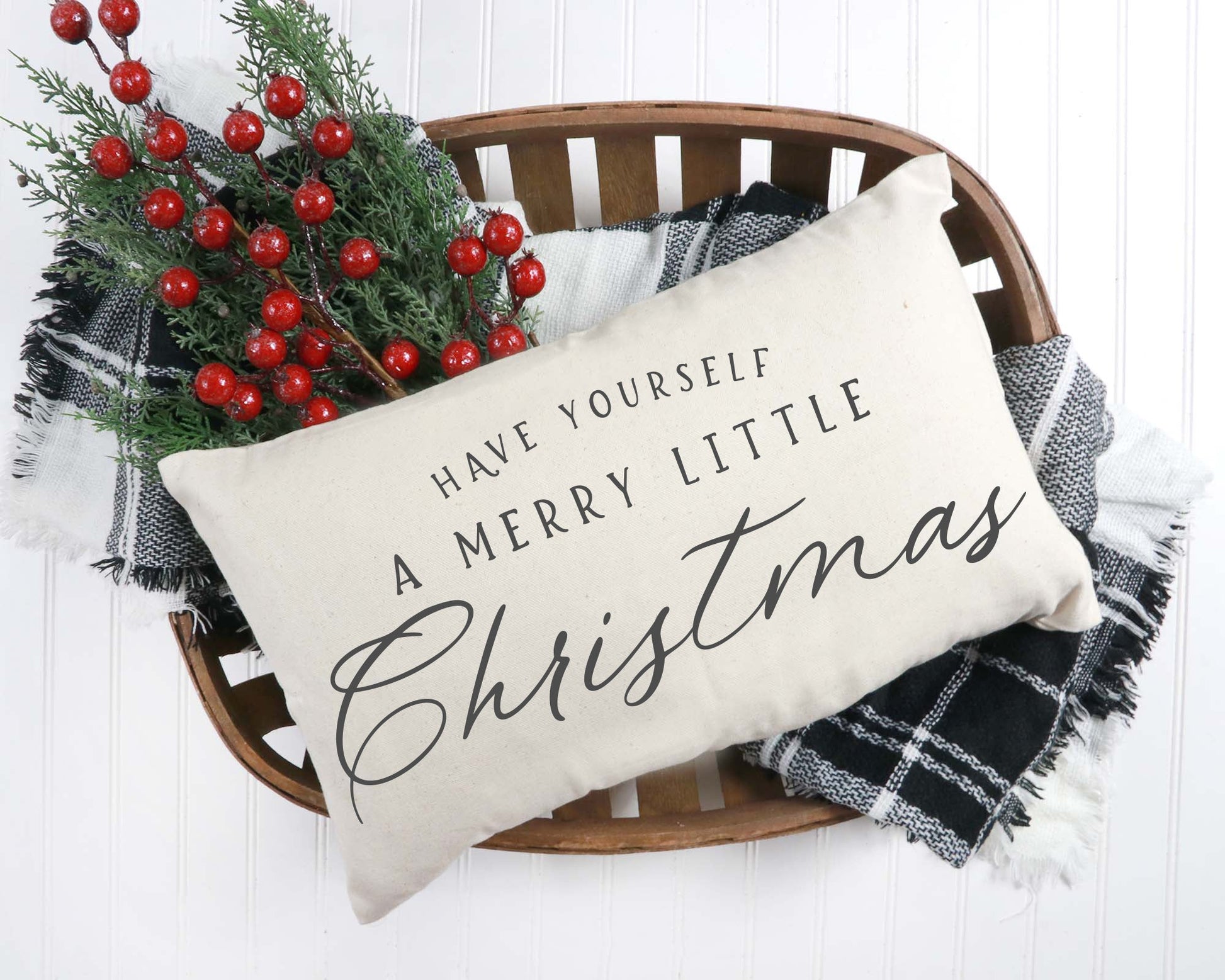 Merry Little Christmas Pillow Cover 12x20 inch on a basket with holiday decorations and cozy blankets.