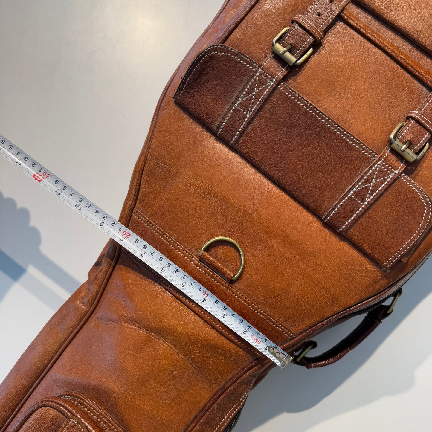 Brown leather bag with a measuring tape for scale on a light gray background