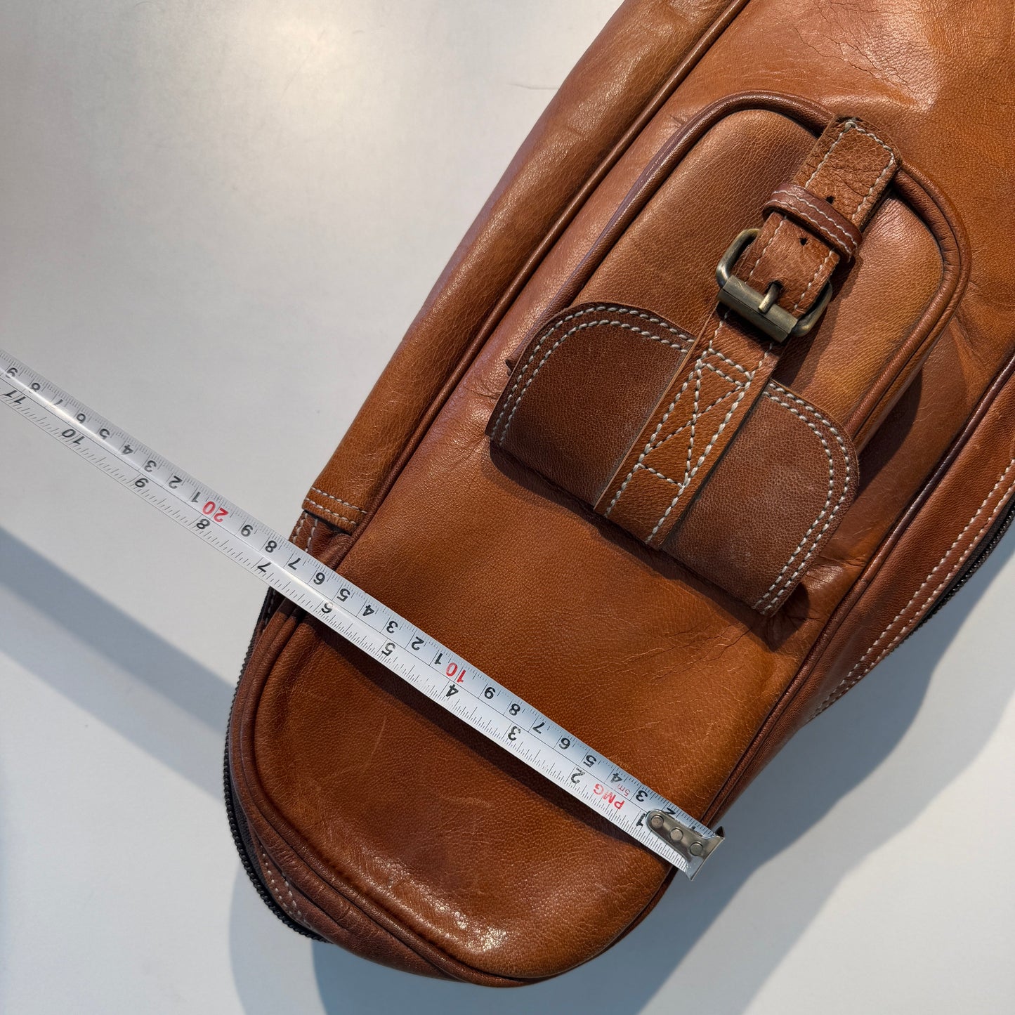 Brown leather bag with a measuring tape for scale on a light gray background