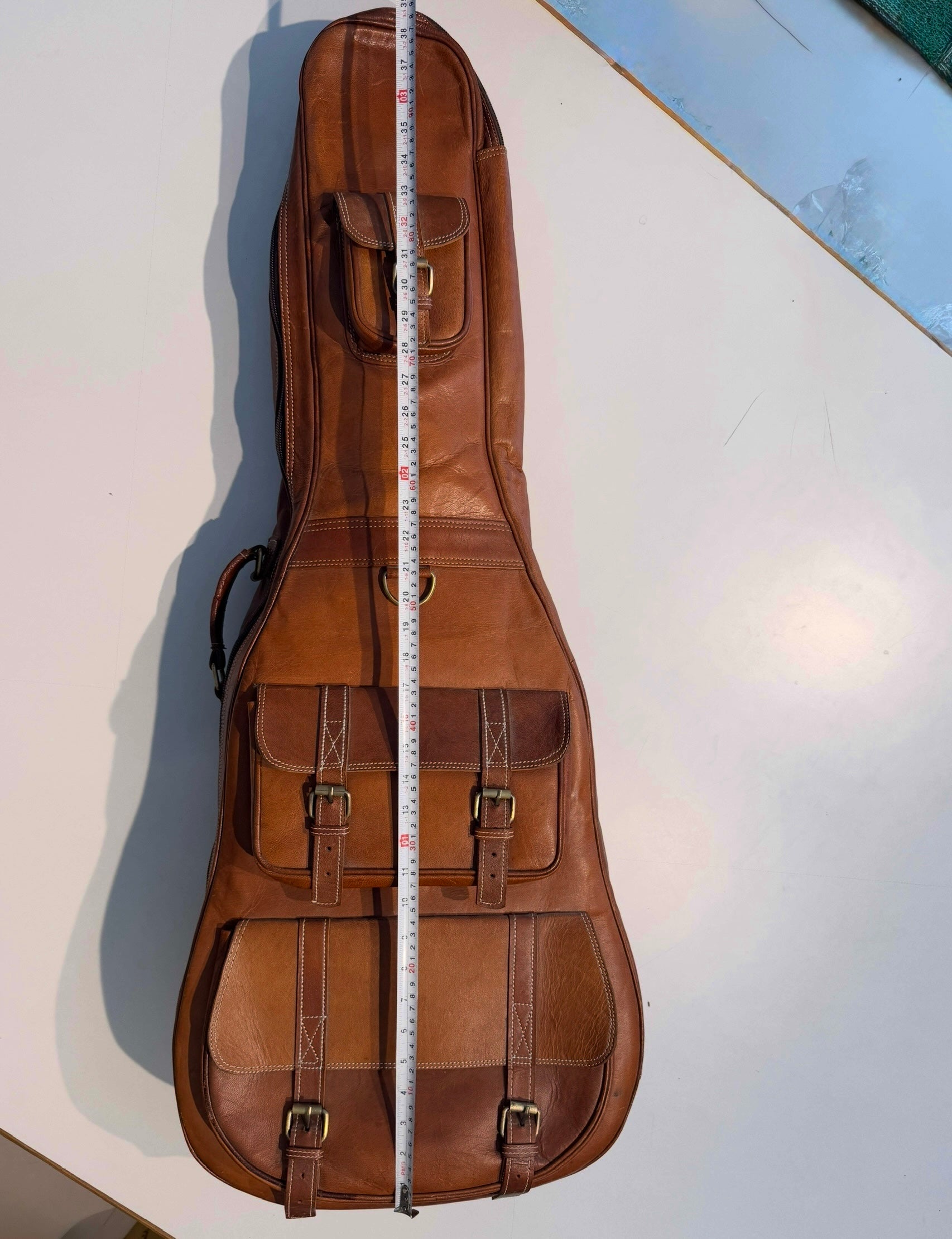 Brown leather guitar case with a measuring tape for scale on a white surface.