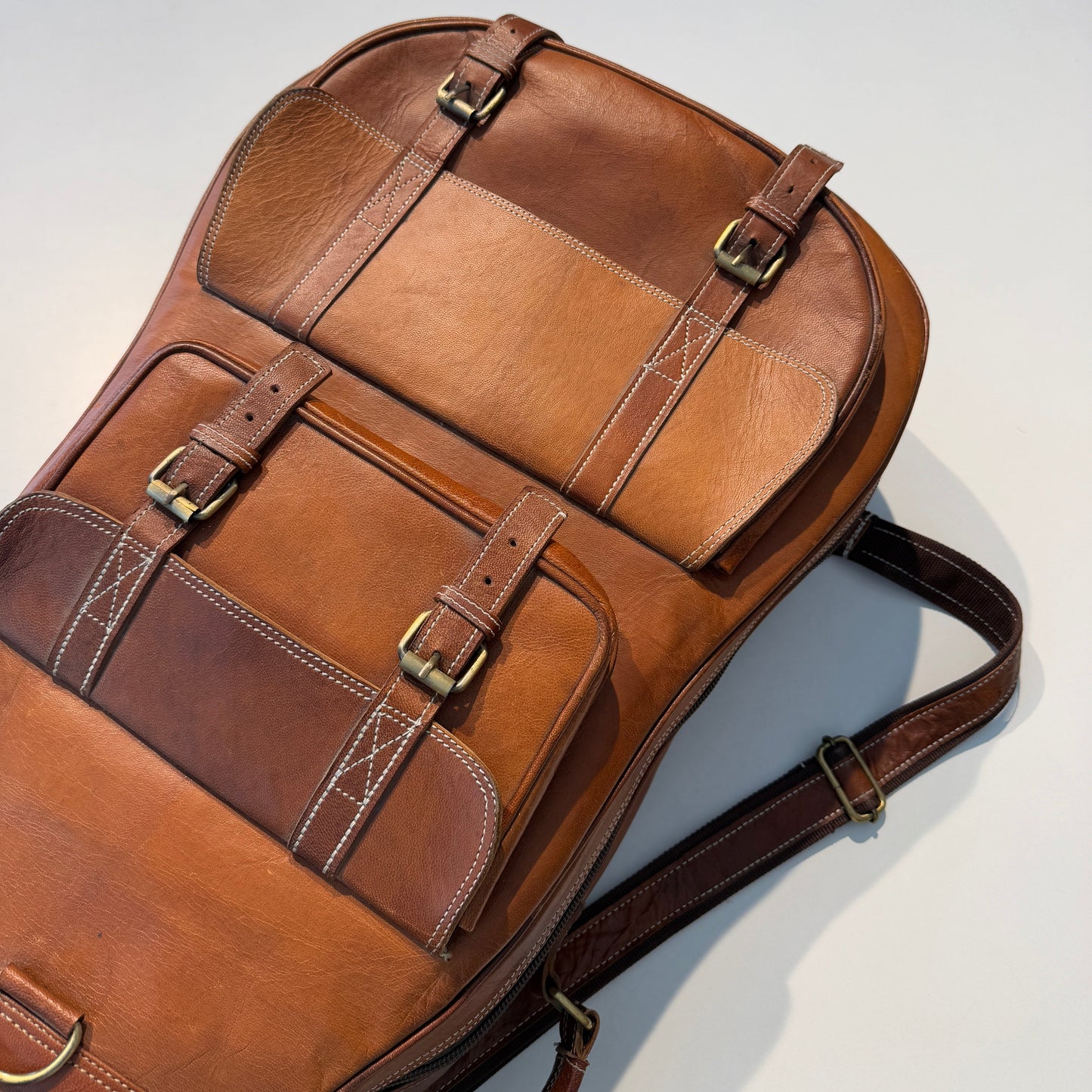 Brown leather backpack with gold buckles on a light gray background