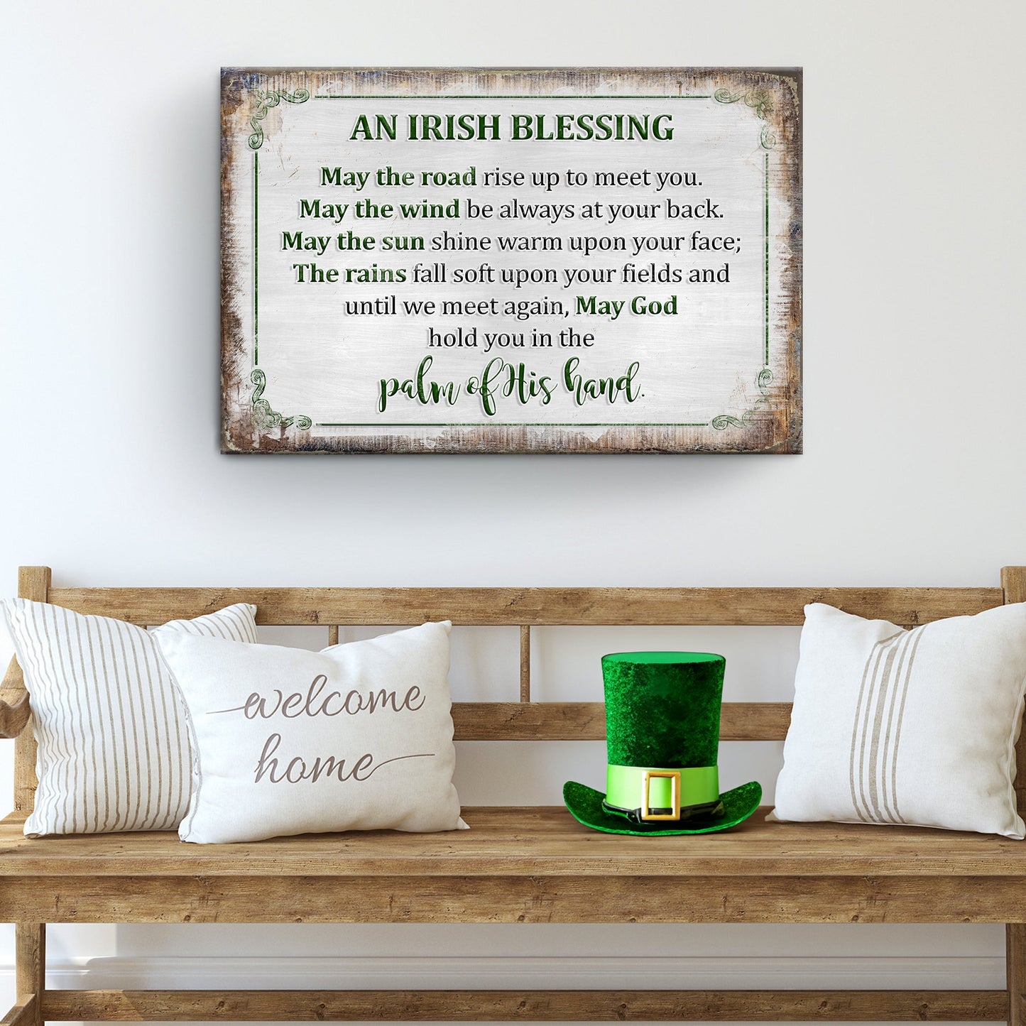 Wooden bench with 'welcome home' pillow, green leprechaun hat, and framed Irish blessing sign on a white wall.