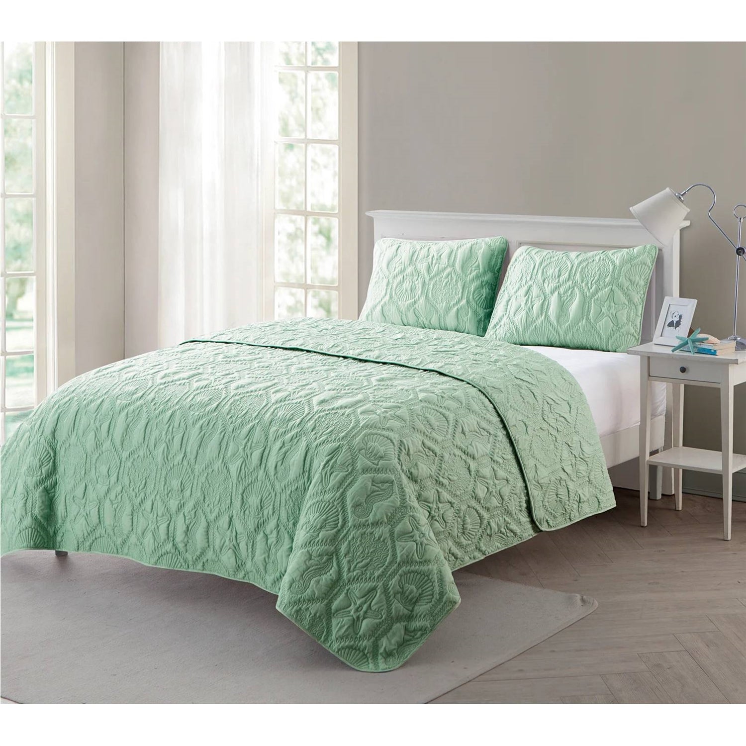 Green quilt set on a bed in a bedroom with a lamp and nightstand.