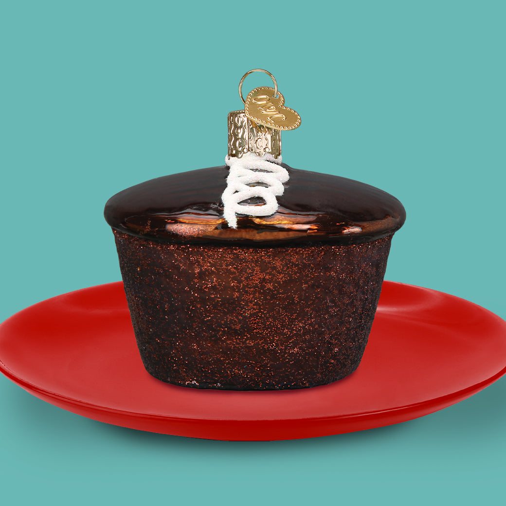 Decorative cupcake ornament with a gold bow on a red plate against a teal background