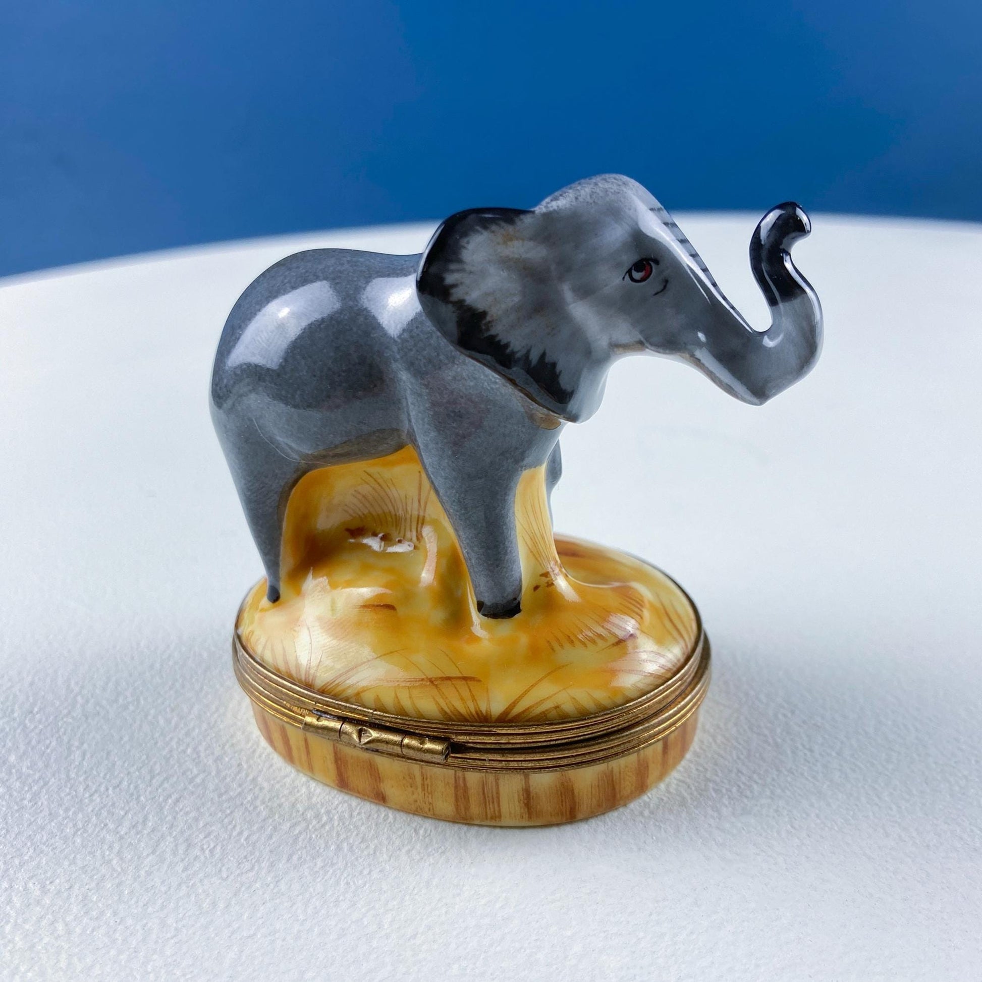Decorative elephant figurine on a round, gold-trimmed box against a blue background