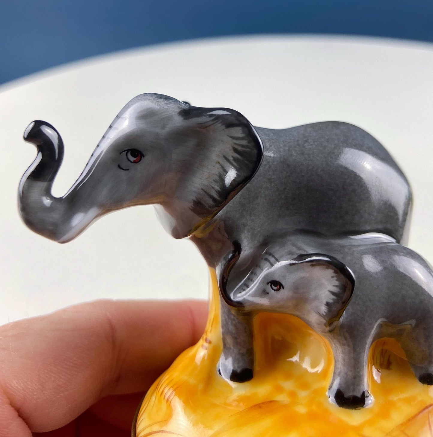 Two elephant figurines on a yellow base held by a hand against a blue background