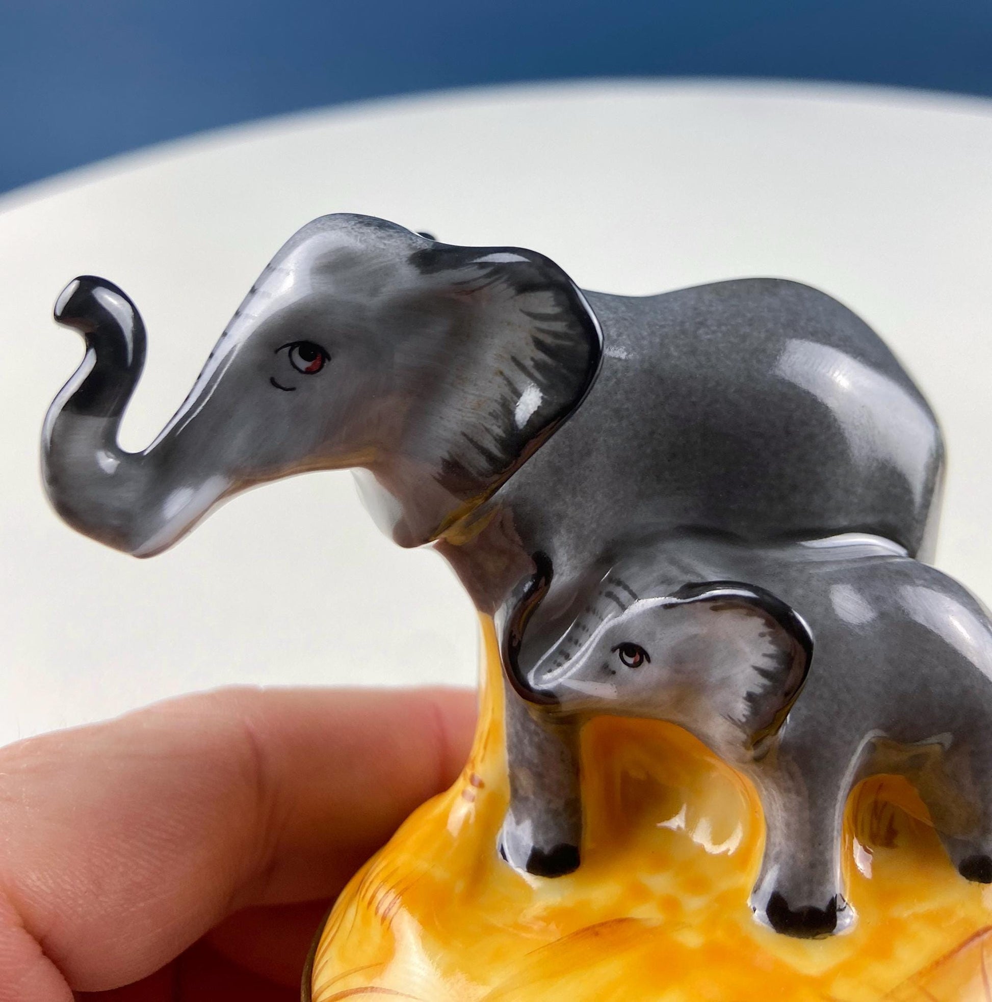 Two elephant figurines on a yellow base held by a hand against a blue background