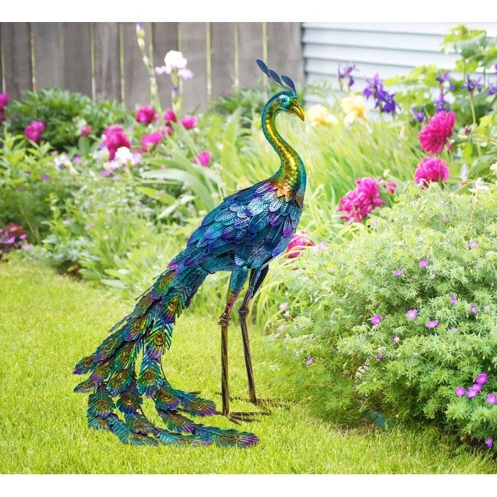 Decorative peacock sculpture in a garden setting with flowers and grass.