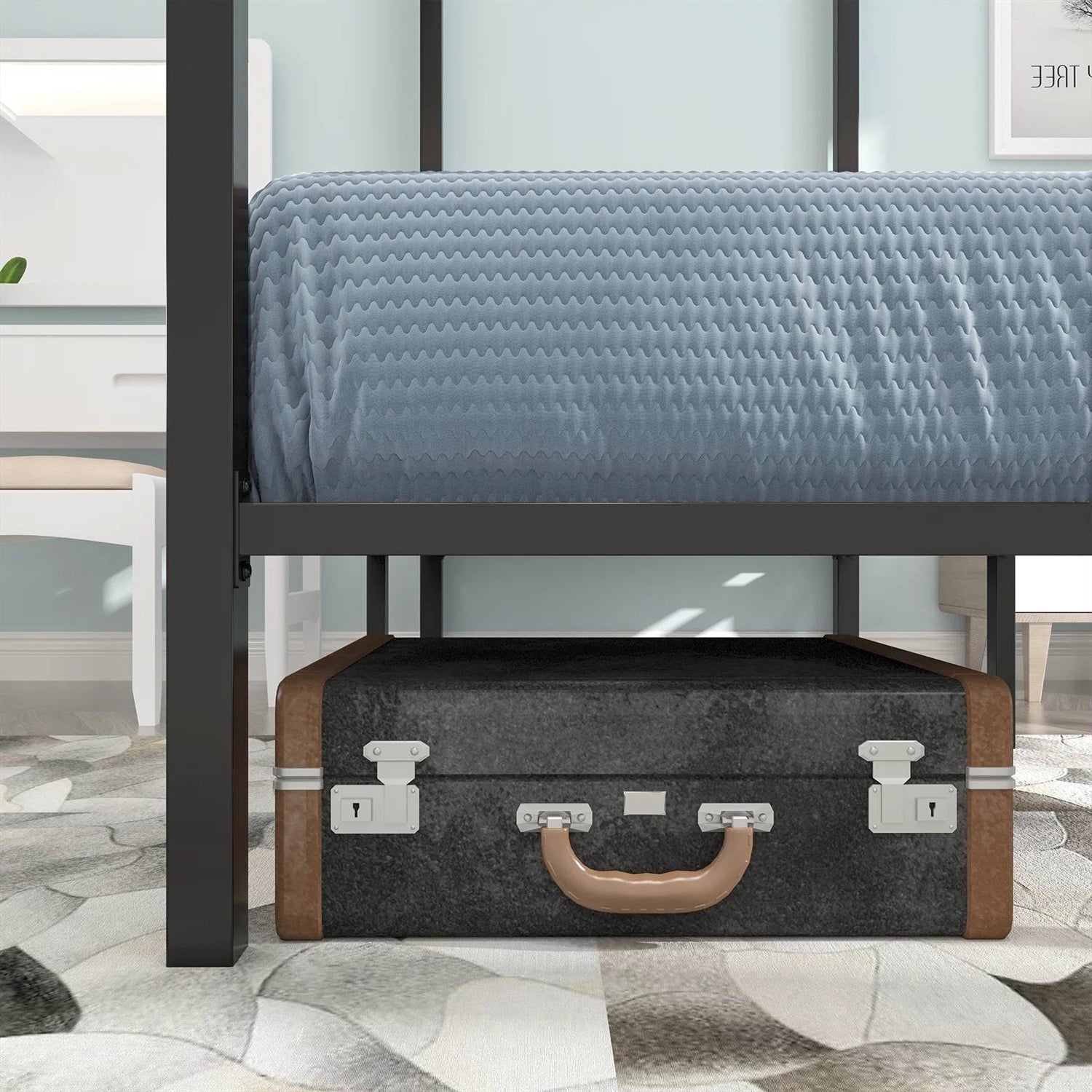 Black metal bed frame with a textured gray mattress and a vintage-style suitcase at the foot of the bed.