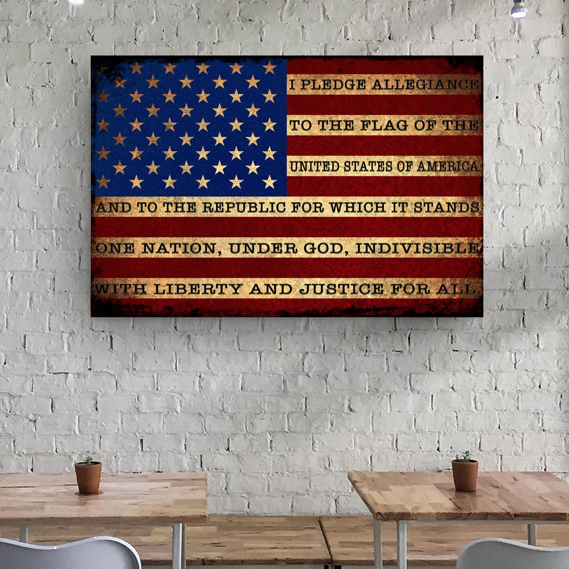 American flag with Pledge of Allegiance on a white brick wall above two wooden tables.