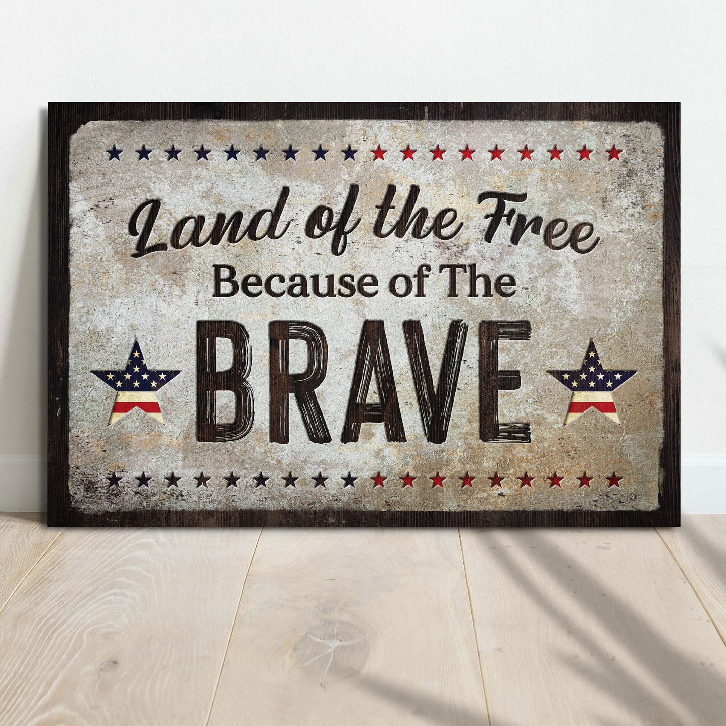 Decorative sign with 'Land of the Free Because of The Brave' text on a wooden floor.