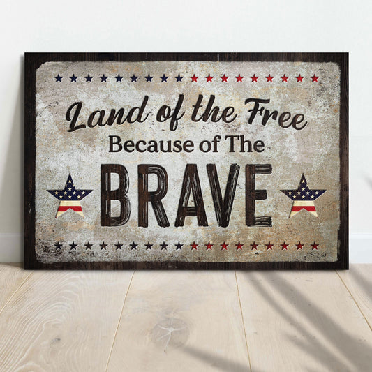Decorative sign with 'Land of the Free Because of The Brave' text on a wooden floor.