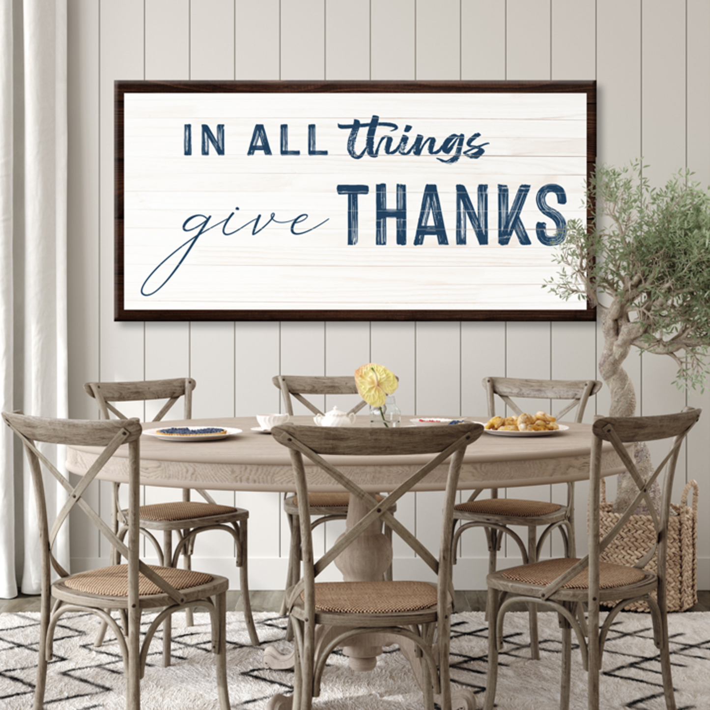 Dining room with a framed sign that reads 'In all things give thanks' on a wooden wall.