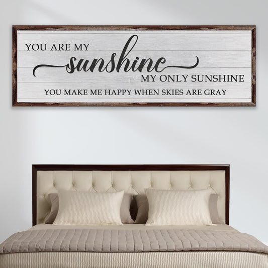 Decorative sign with 'You are my sunshine' text above a bed with a wooden headboard.