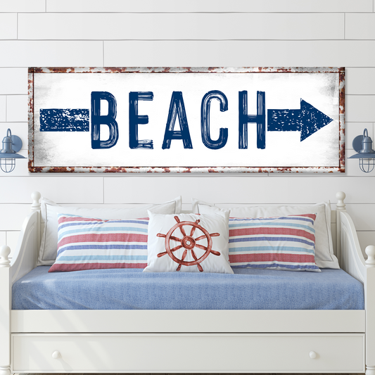 Decorative sign with 'BEACH' and an arrow above a bed with nautical-themed pillows.