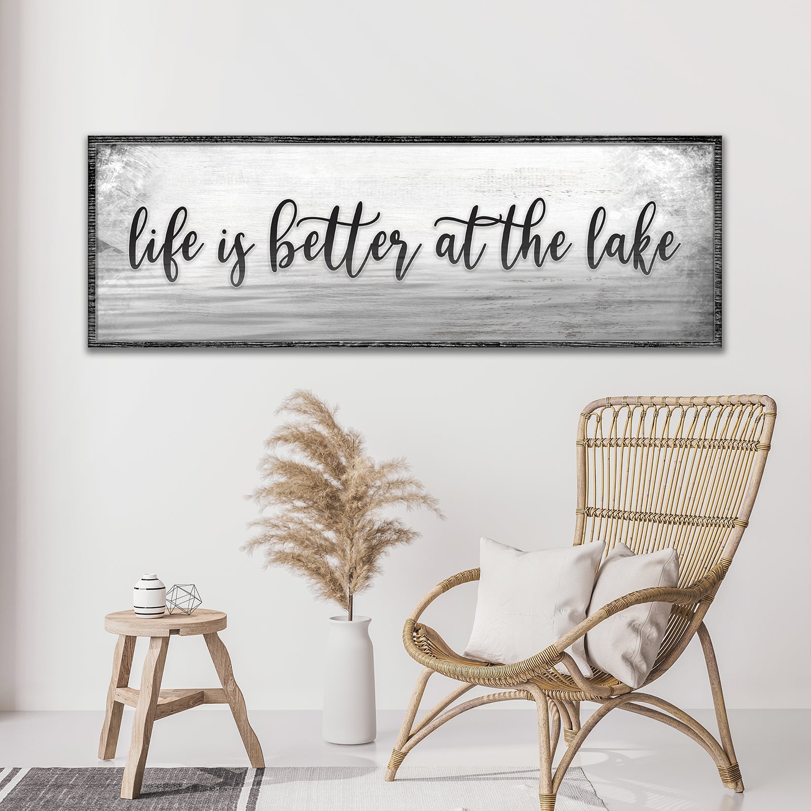 Decorative sign with 'life is better at the lake' text in a room with a wicker chair and potted plant.