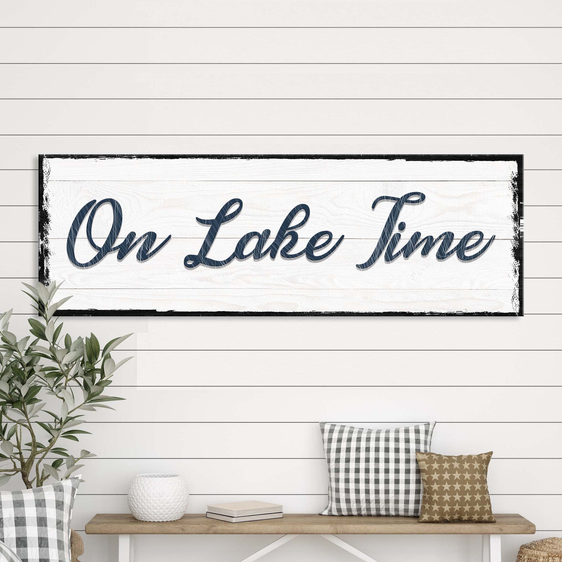 Decorative sign with 'On Lake Time' text in a rustic setting with a plant and bench.