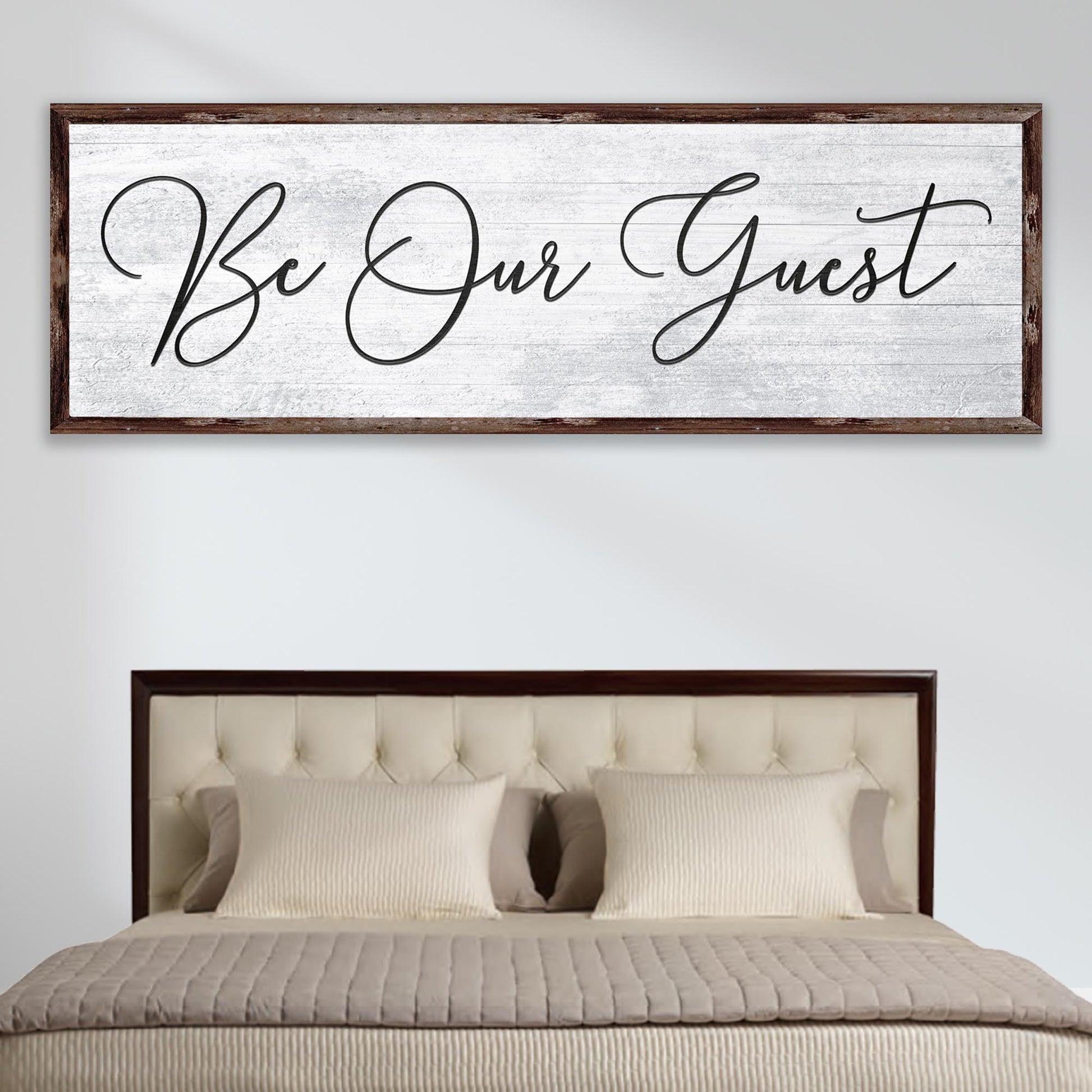 Decorative wall sign with 'Be Our Guest' text above a bed in a bedroom setting.