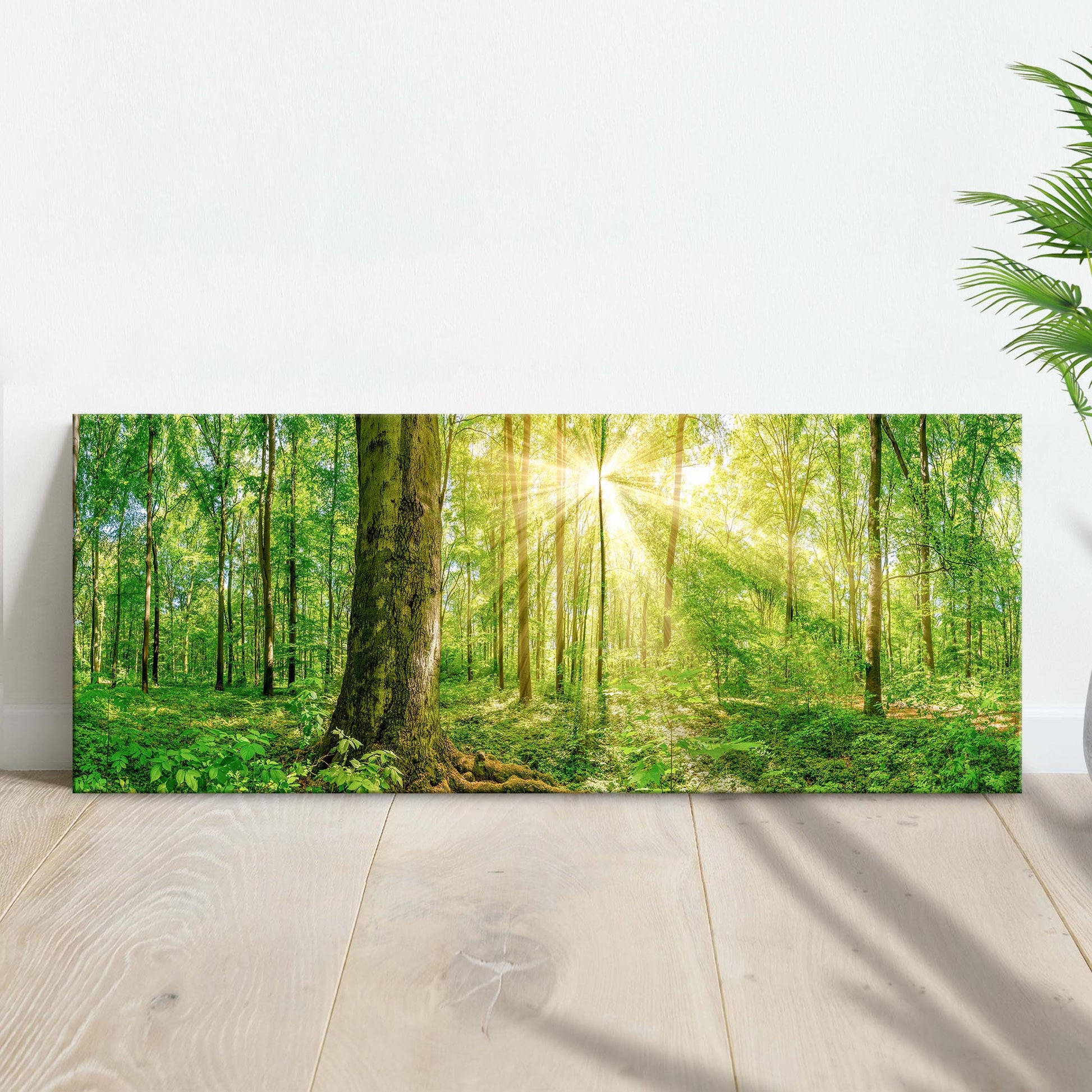 Canvas print of a forest scene with sunlight filtering through the trees, placed on a wooden floor.