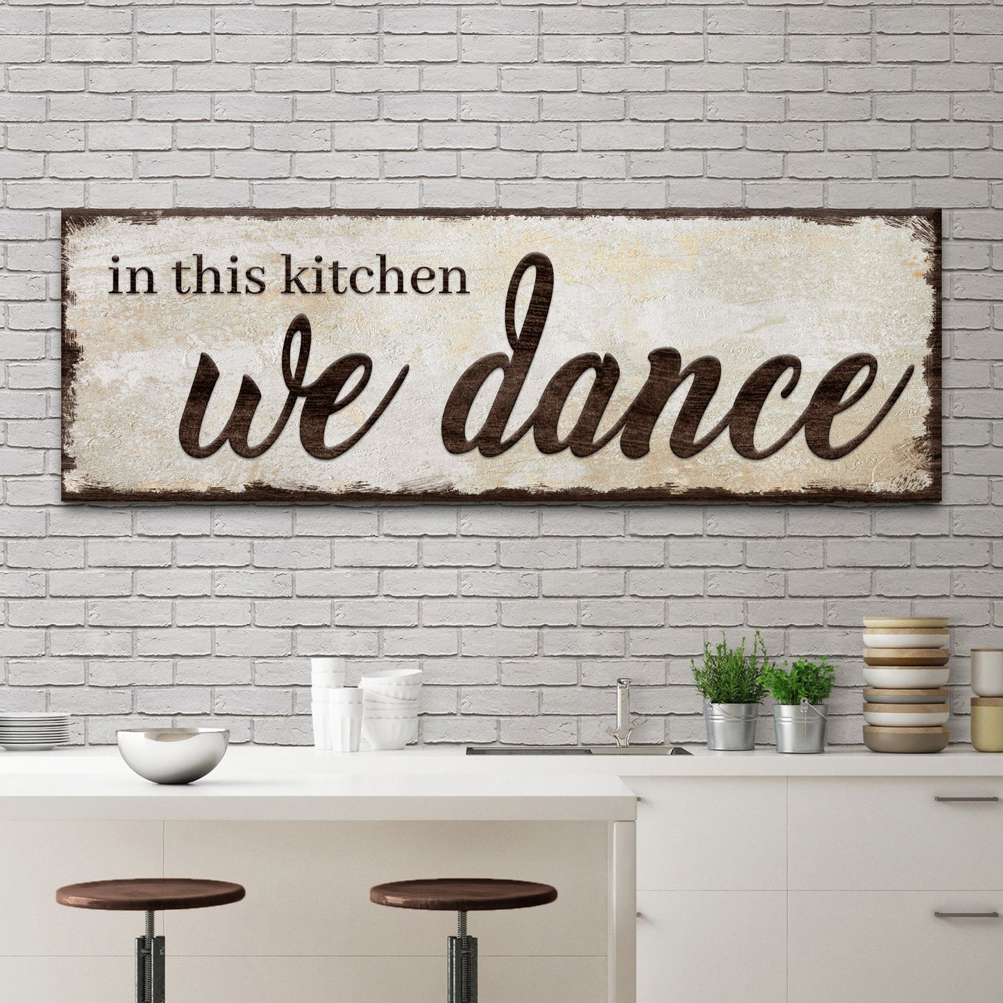 Decorative sign with 'in this kitchen we dance' text in a kitchen setting.