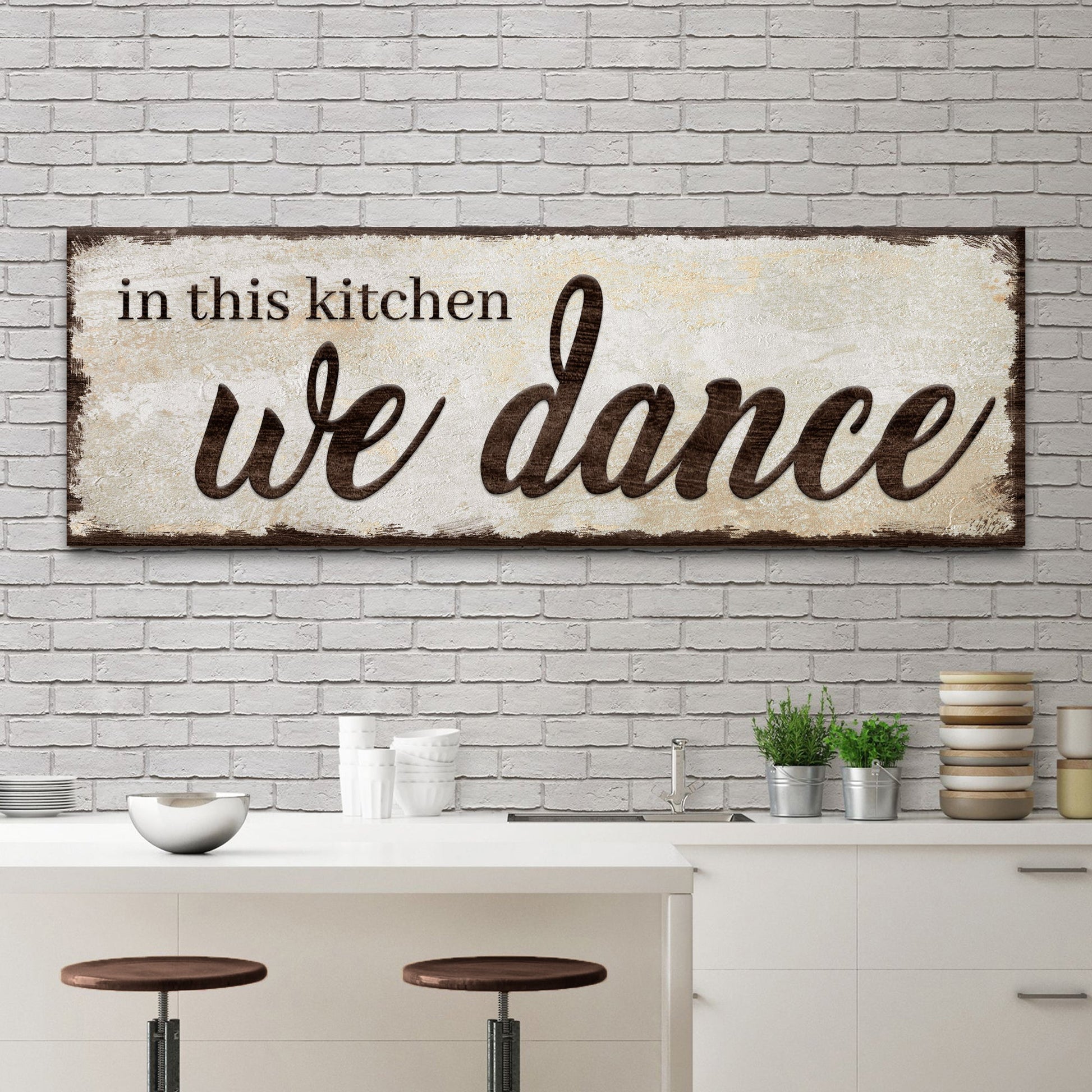 Decorative sign with 'in this kitchen we dance' text in a kitchen setting.