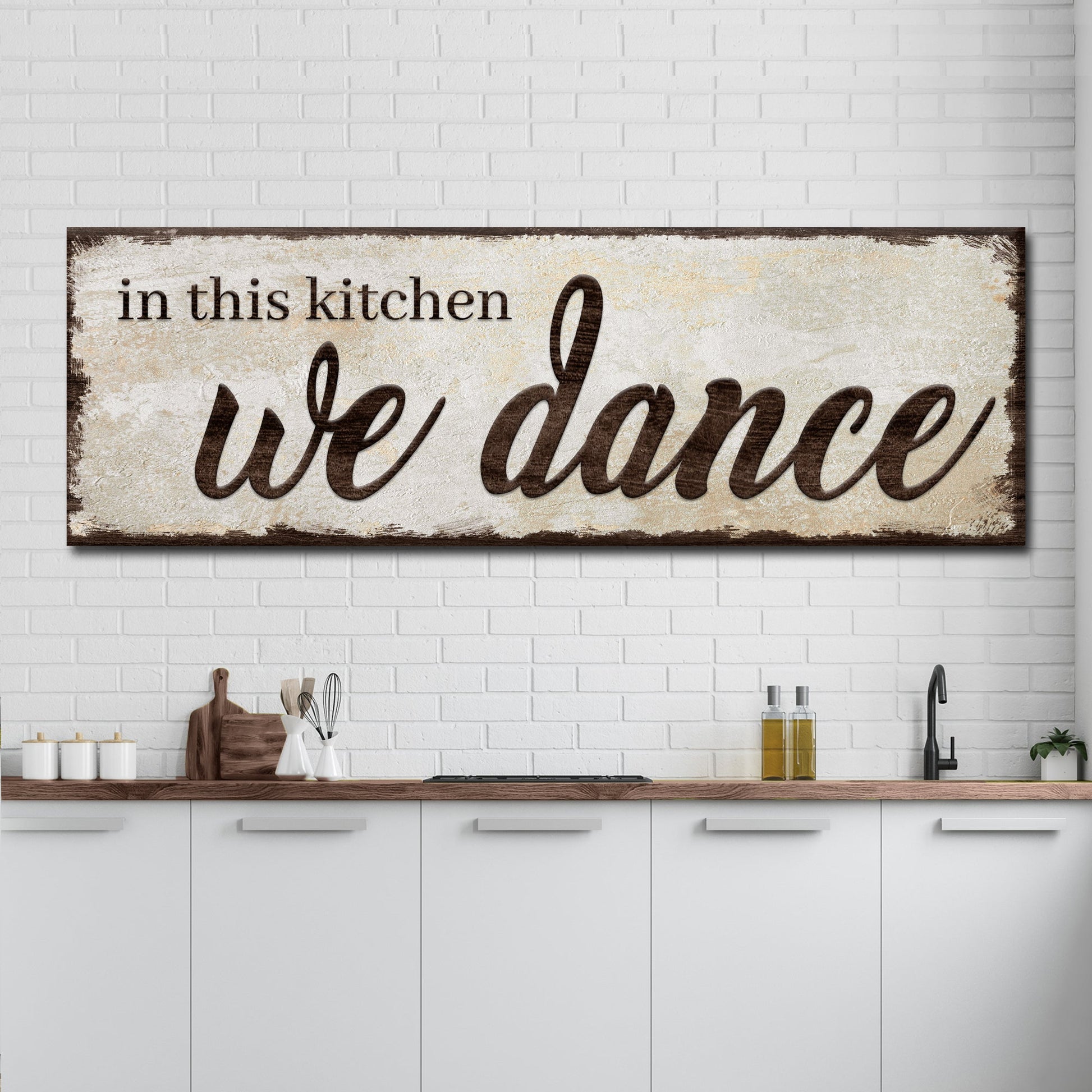 Decorative sign with 'in this kitchen we dance' text in a kitchen setting.