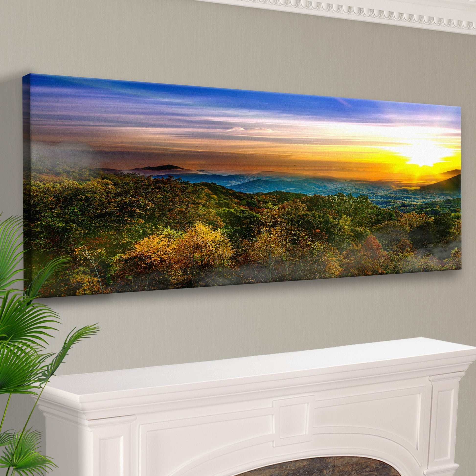 Panoramic landscape print of a sunset over a forest above a white fireplace.