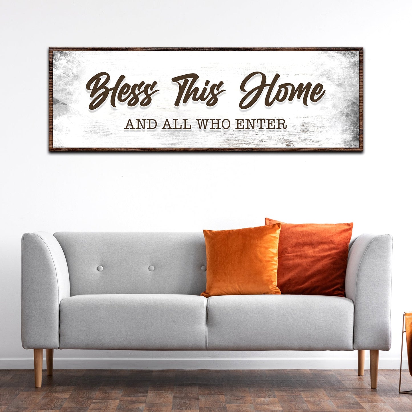 Decorative sign above a gray sofa with orange pillows in a living room setting.
