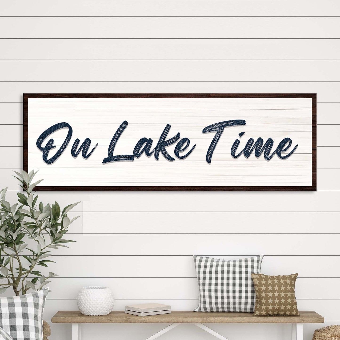 Framed artwork with 'On Lake Time' text on a wall above a bench with decorative pillows.