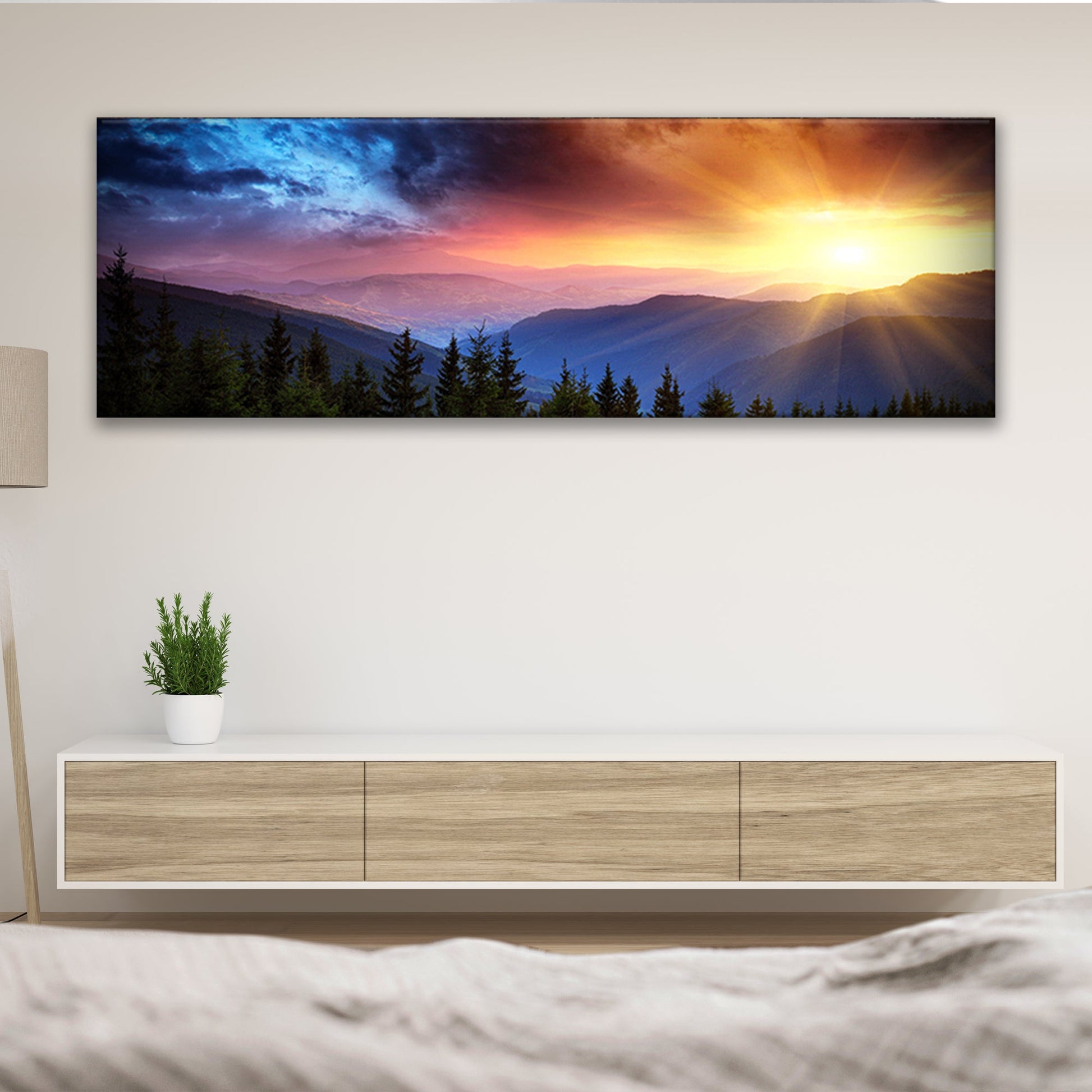 Panoramic landscape print of a sunset over mountains on a wall above a wooden console table.